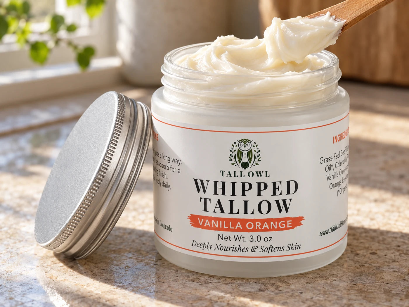Open 3 oz Vanilla Orange Whipped Tallow jar with cream on a wooden spatula and its silver lid beside it